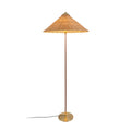 Clérachic floor lamp with a glowing woven rattan cone shade, a dark stem and a black cord trailing left, on white.