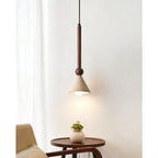 A beige travertine cone pendant on a walnut stem glows warmly beside a pale curtain, above a small round side table, from Clérachic.