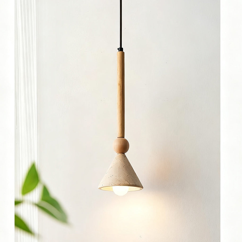 Light wooden stem and bead holding a travertine cone shade against a pale wall, with a green leaf out of focus, from Clérachic.