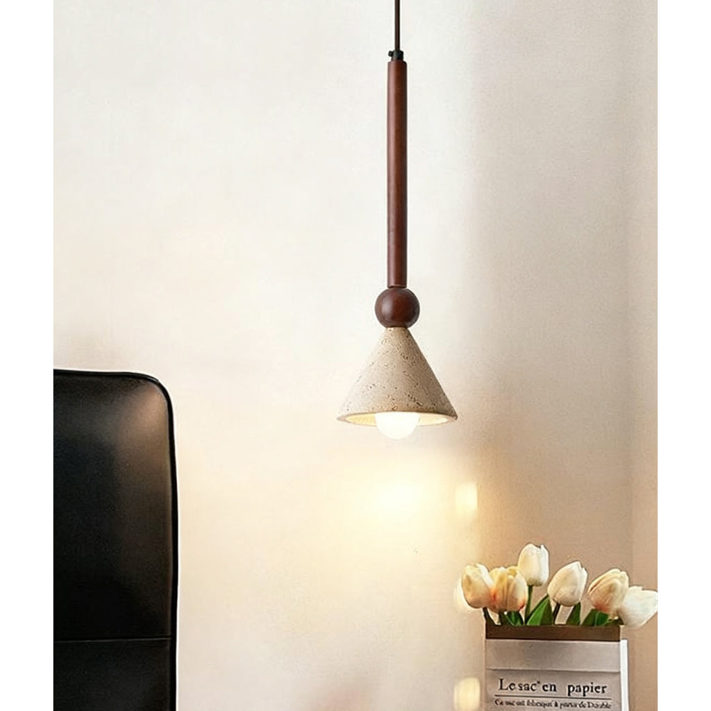 Over a vase of white tulips and a black chair, a travertine cone pendant on a walnut stem hangs against a cream wall, from Clérachic.