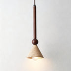 A travertine cone pendant on a walnut stem and a round bead, its warm bulb lit, hangs against a plain pale wall, from Clérachic.