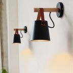 Two black Clérachic wall lights in different sizes on a pale wall, each shade casting a warm pool of light below.