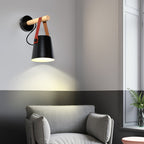 Black Clérachic wall light glowing above a grey armchair, with a two-tone wall in grey and charcoal and a window beside it.