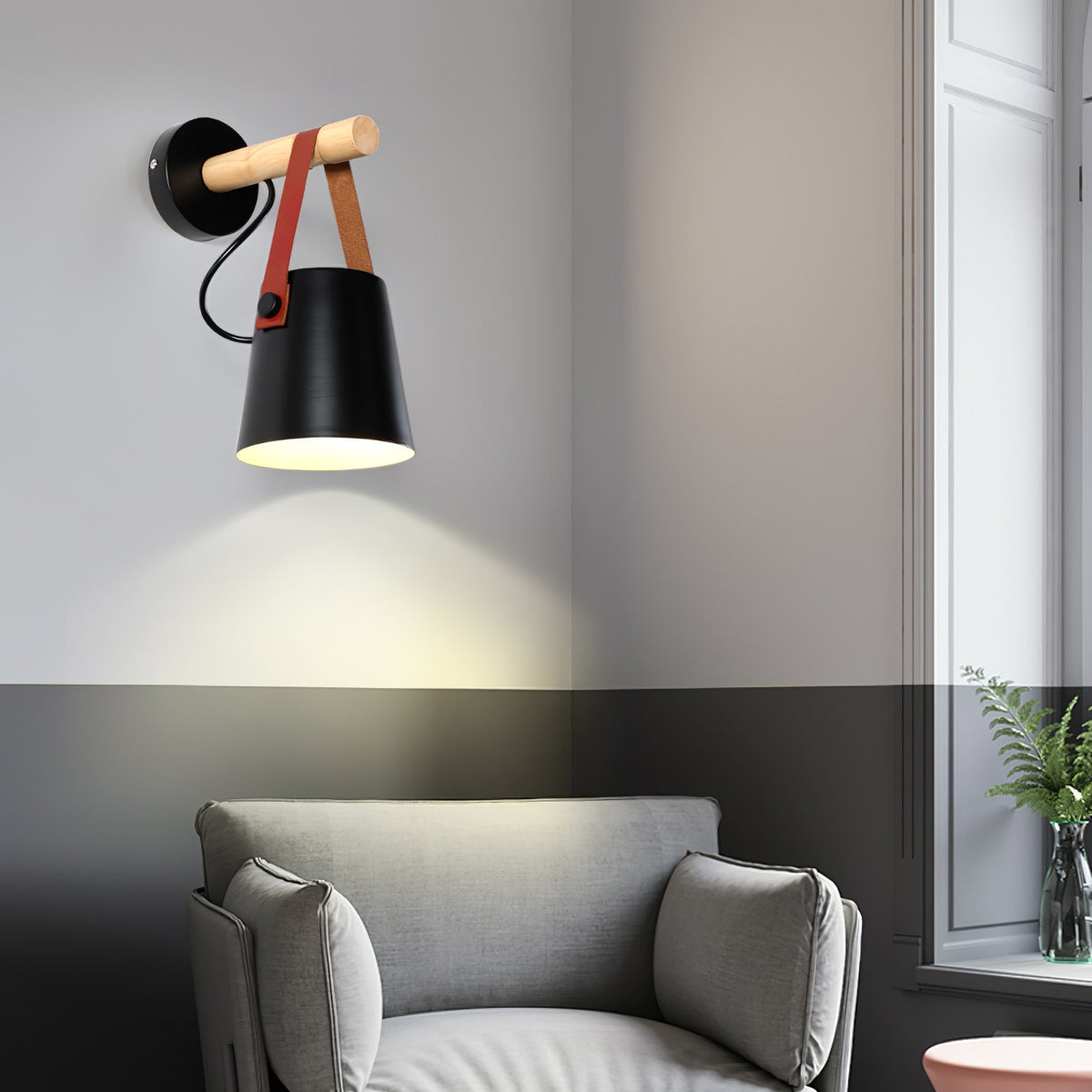 Black Clérachic wall light glowing above a grey armchair, with a two-tone wall in grey and charcoal and a window beside it.