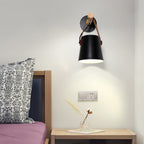 Black Clérachic wall light above a wooden bedside table with a dried-flower vase, beside a bed with a patterned cushion.