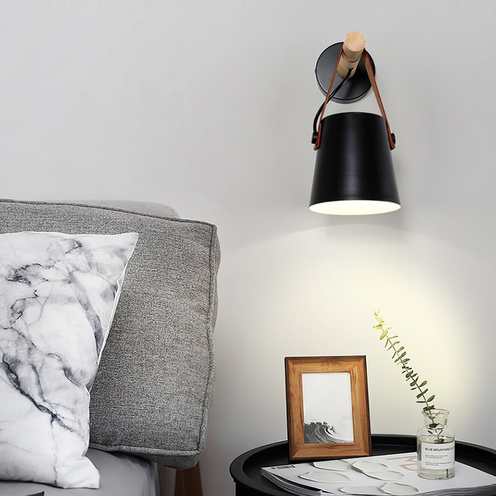 Black Clérachic wall light lighting a grey wall, above a framed picture and a round black side table beside a grey sofa.