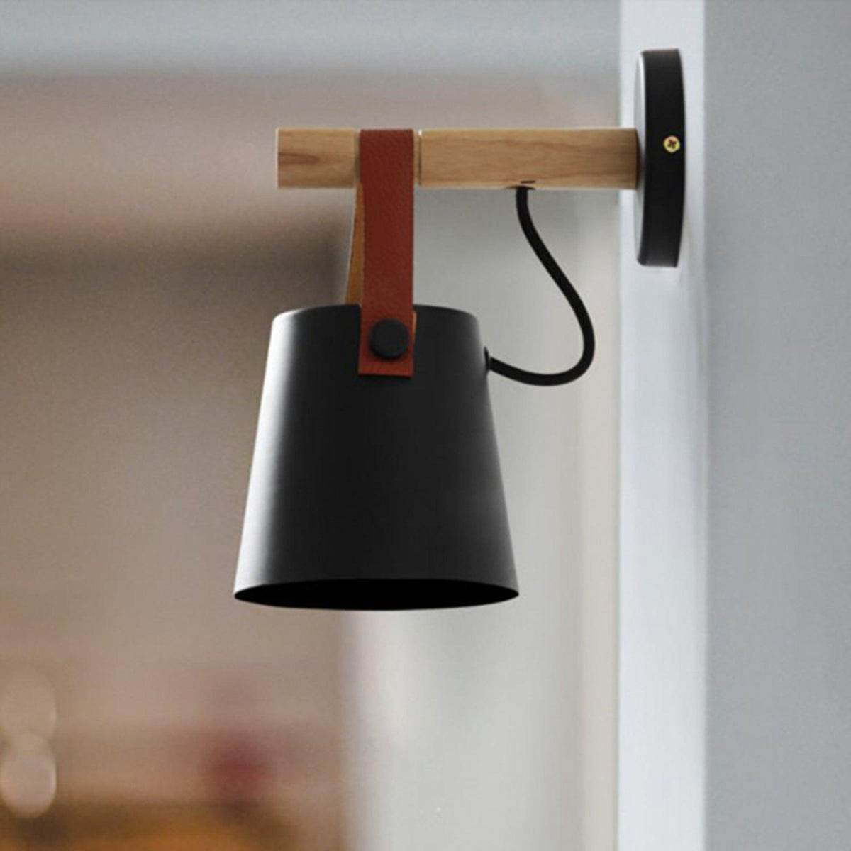 Side view of a black Clérachic wall light on a pale wall, the leather strap fixed with a button to the shade.
