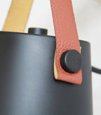 Close view of the tan leather strap and black button where it joins the black shade on this Clérachic wall light.