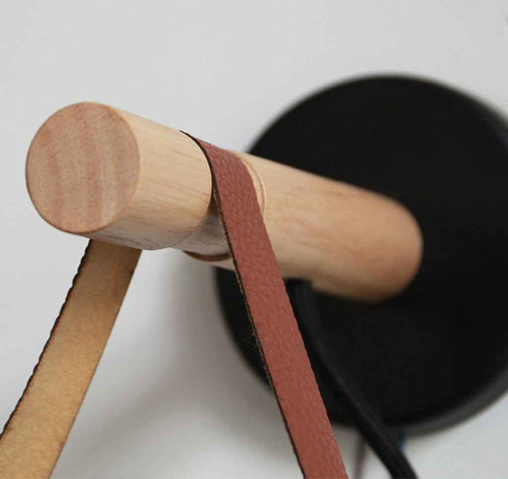 Close view of the round wooden bar, leather strap and black wall plate of this Clérachic wall light.