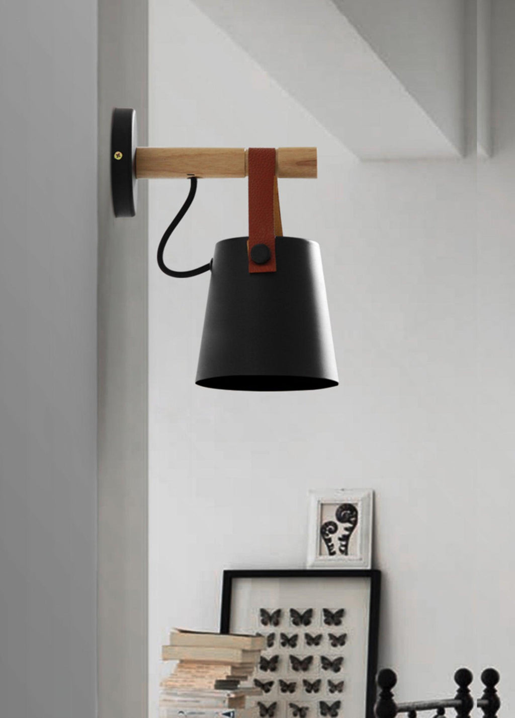 Black Clérachic wall light on a pale wall above a shelf of books and a framed butterfly print.
