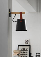 Black Clérachic wall light on a pale wall above a shelf of books and a framed butterfly print.