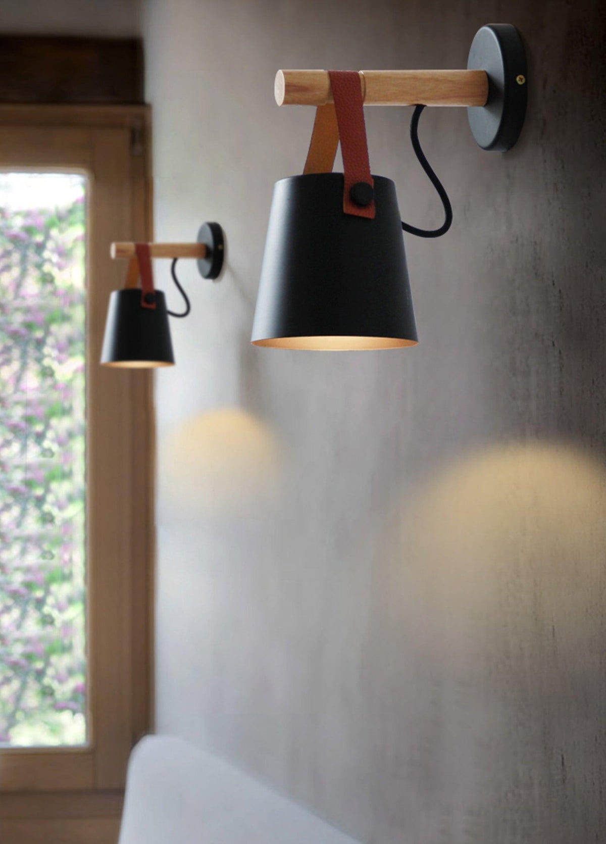 Two black Clérachic wall lights, one near and one far, on a grey wall beside a small window.