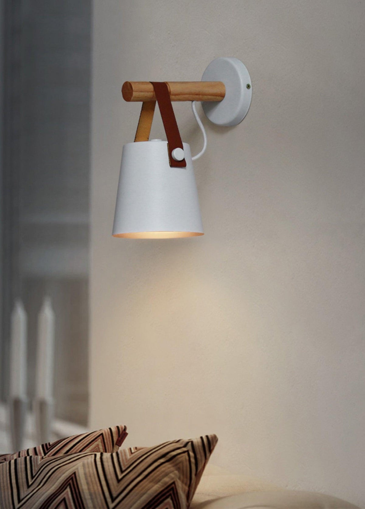 White Clérachic wall light on a warm grey wall above a sofa with zigzag-patterned cushions.