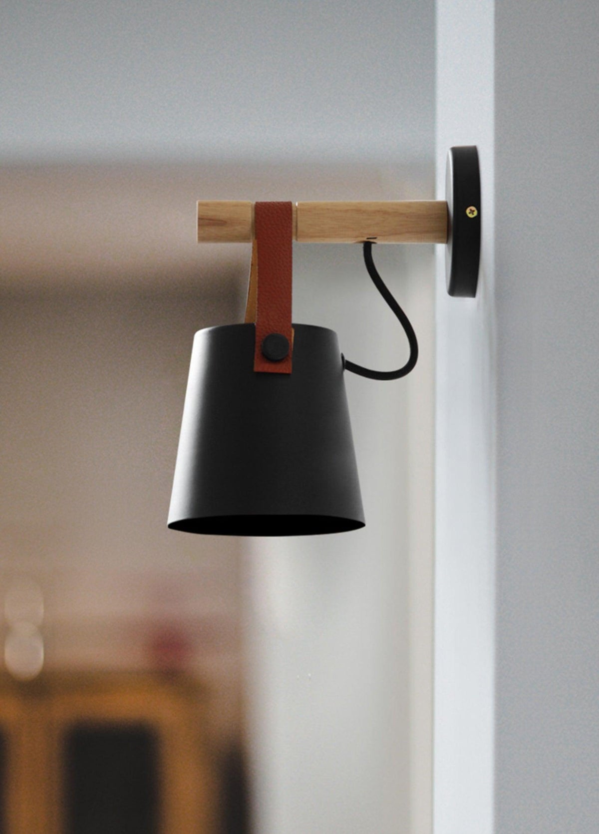 Black Clérachic wall light seen side-on against a soft-focus interior, the cord curving from the shade to the wall plate.