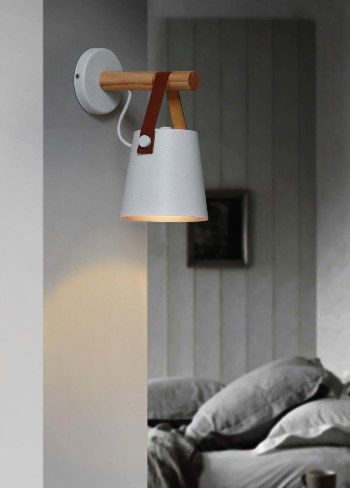 White Clérachic wall light on a grey panelled wall above a bed with grey bedding and a framed picture.