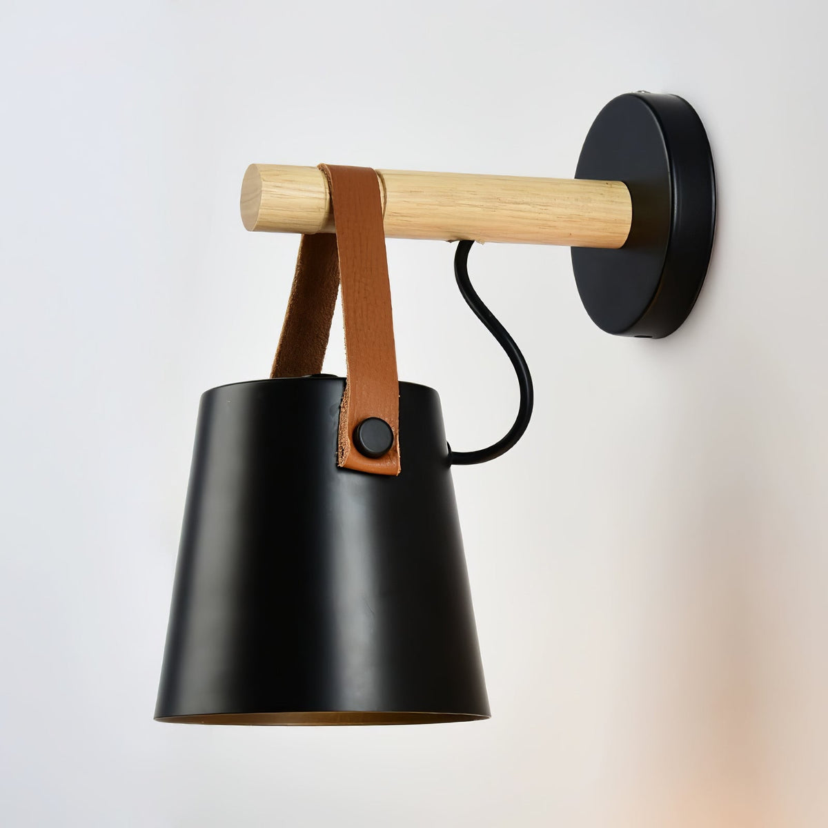 Black Clérachic wall light viewed from the front, its tan strap held by a black button on the shade.