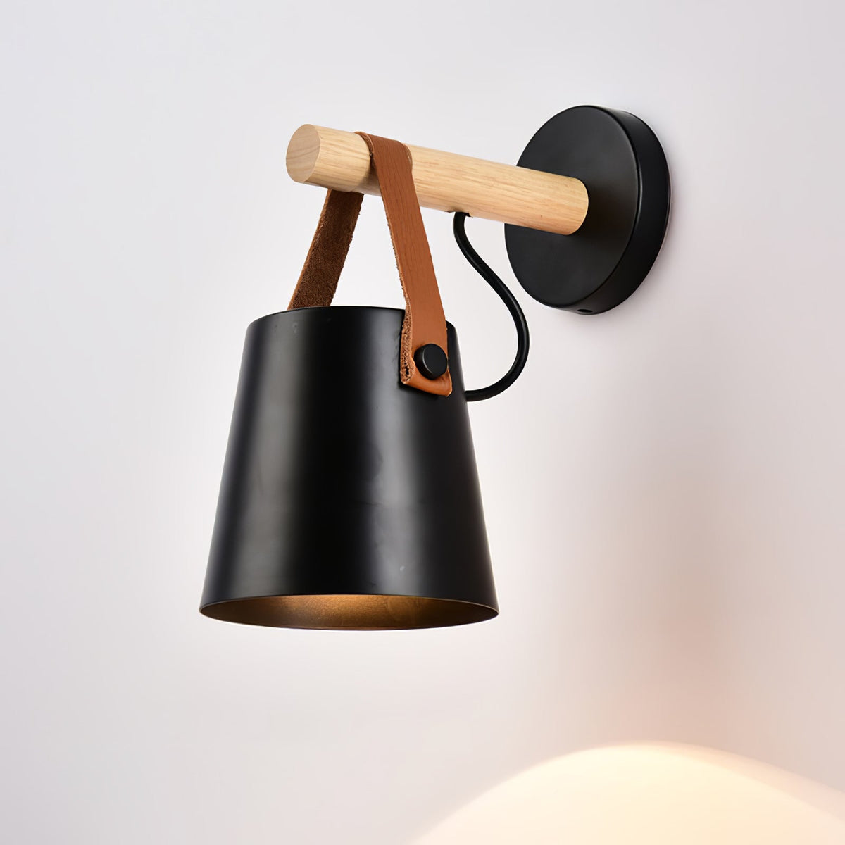 Black Clérachic wall light on a pale wall, its lit opening throwing a faint glow onto the wall below.