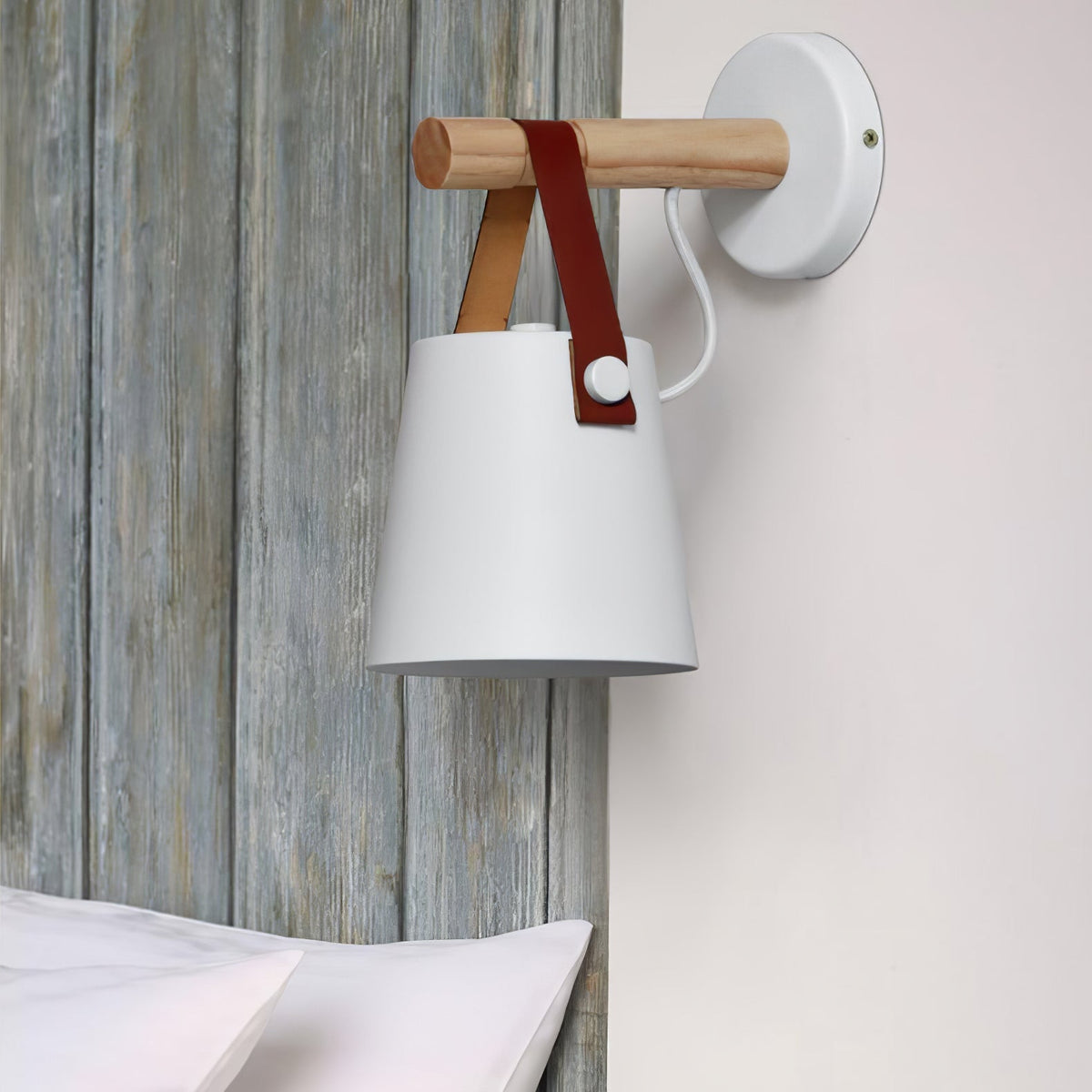 White Clérachic wall light on a pale wall next to a grey wooden panel, with white bedding at the bottom edge.