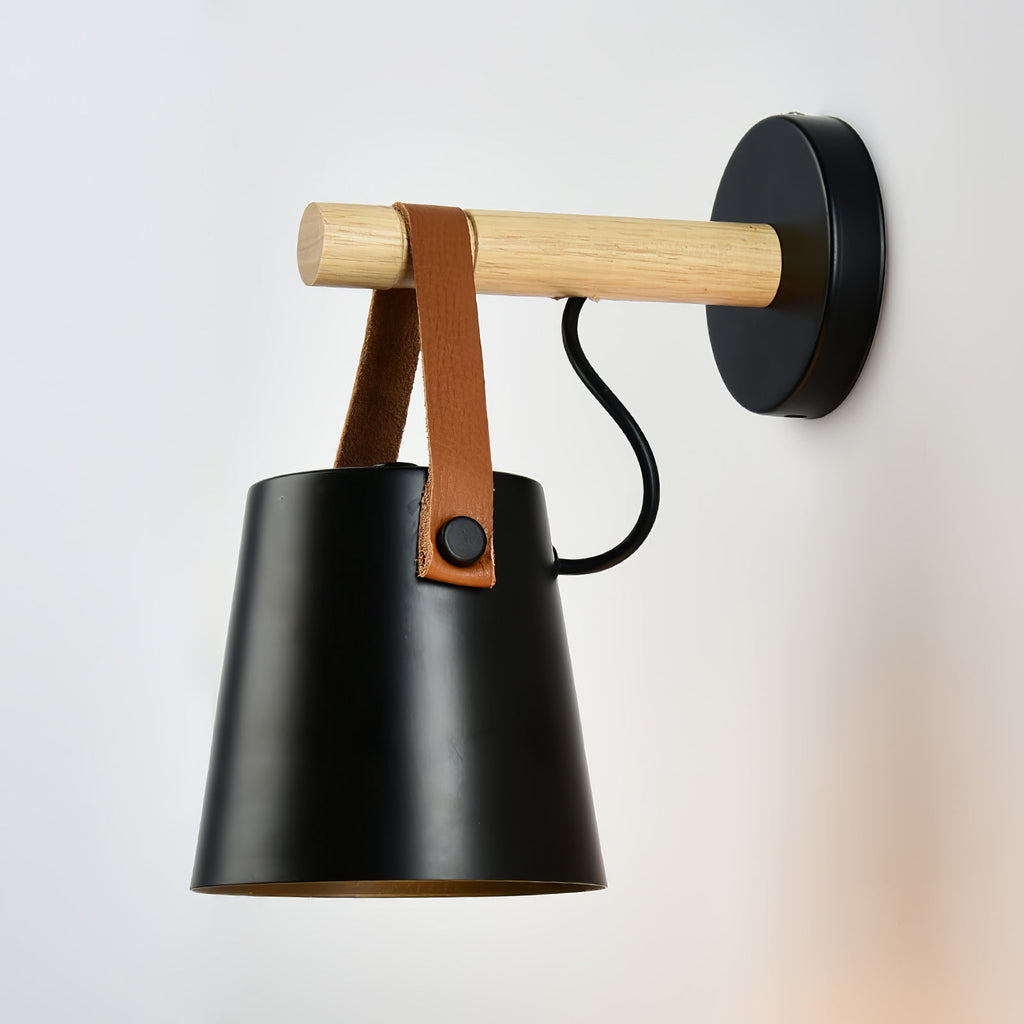 Black Clérachic wall light angled to show its inner shade, with a pale wooden bar and a brown leather strap.