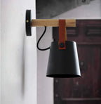 Black Clérachic wall light on a white wall beside a dark red wooden door, seen from the side with its black cord.