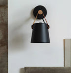 Black Clérachic wall light hanging from a round black wall plate on a pale wall with a wooden edge and a ledge below.