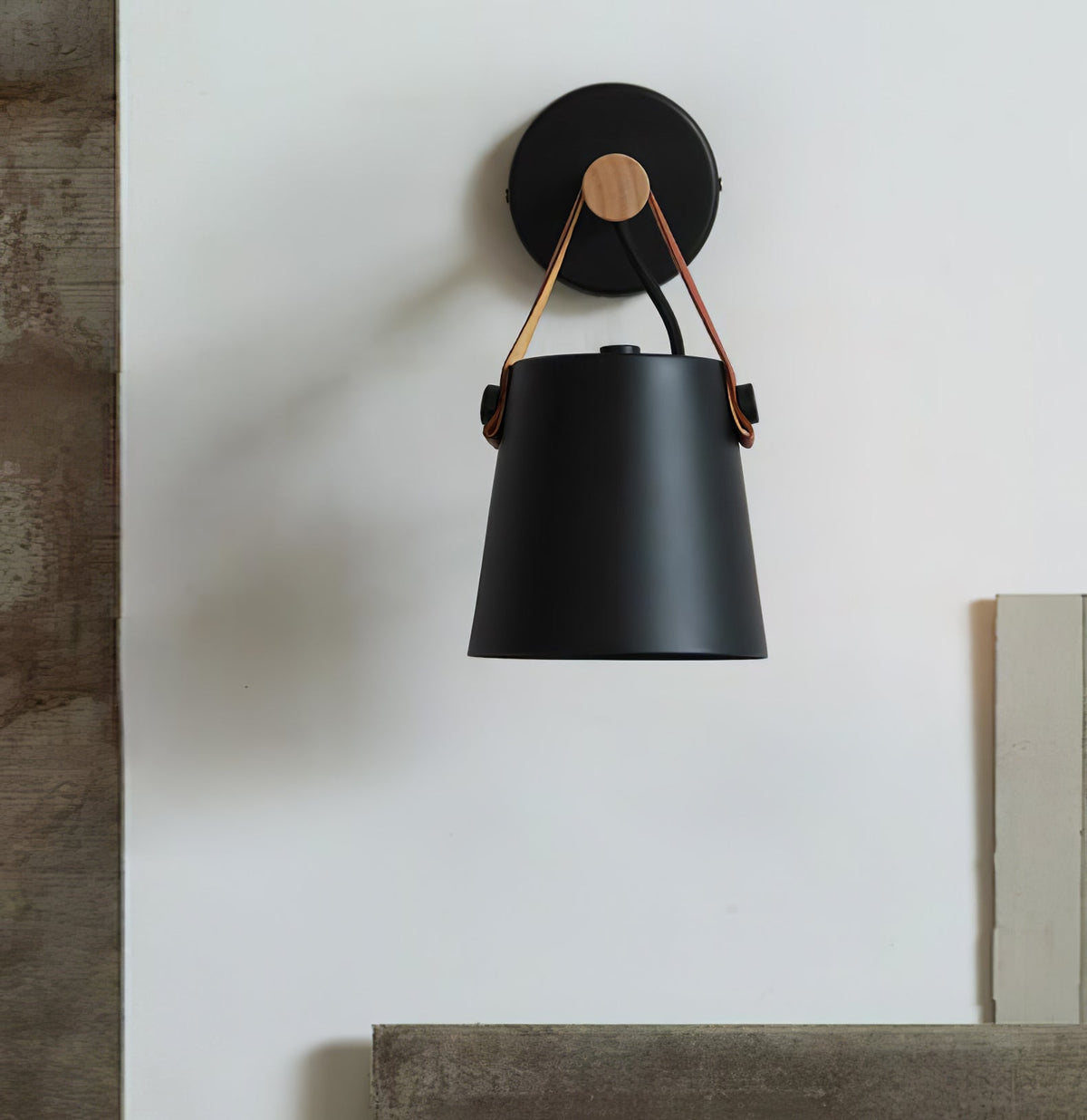 Black Clérachic wall light hanging from a round black wall plate on a pale wall with a wooden edge and a ledge below.