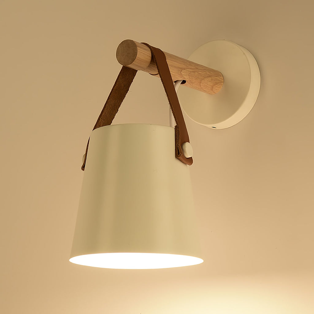 White Clérachic wall light glowing in warm light on a golden wall, with the wooden bar and strap at the top.