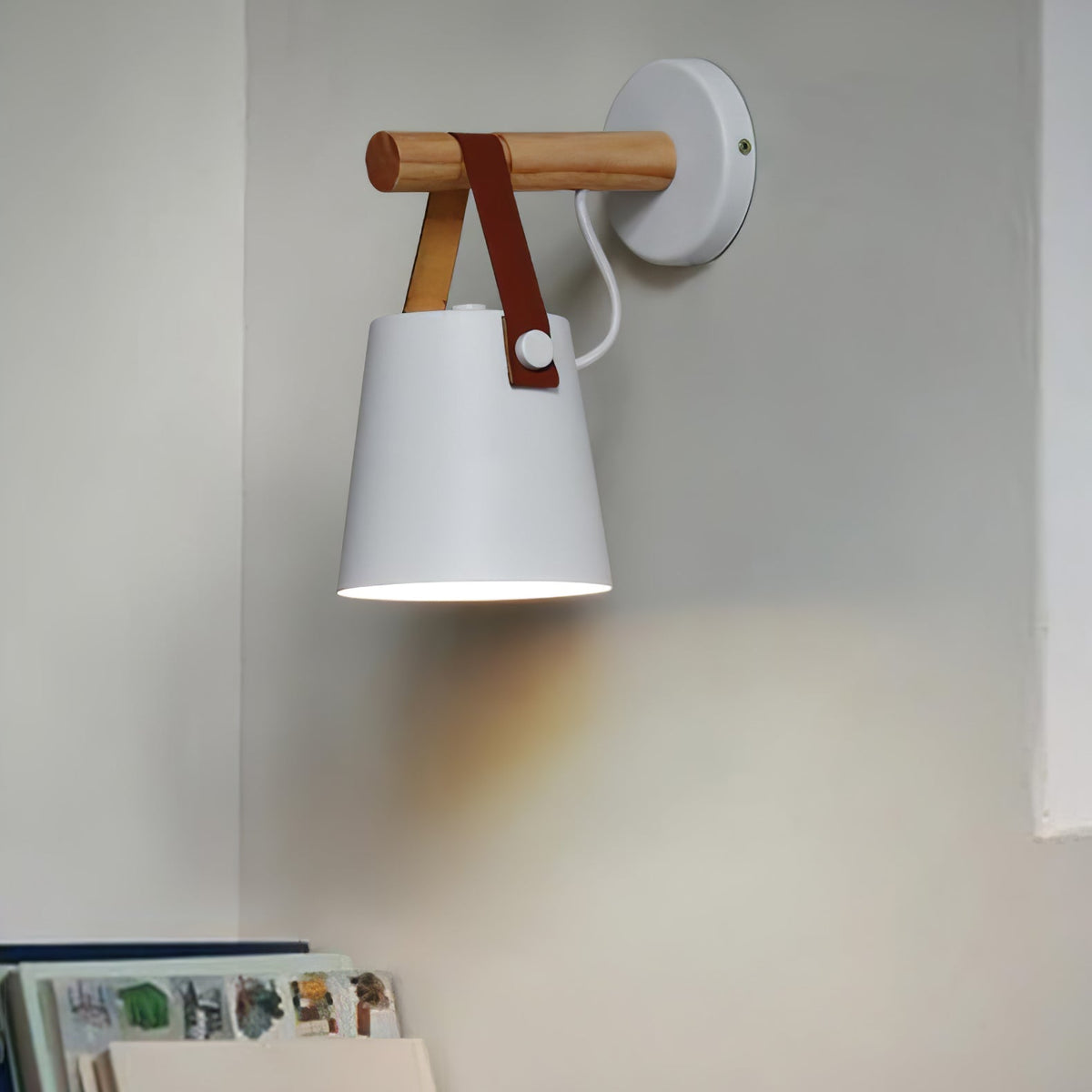 White Clérachic wall light lighting a grey corner, above a shelf of picture books at the lower left.