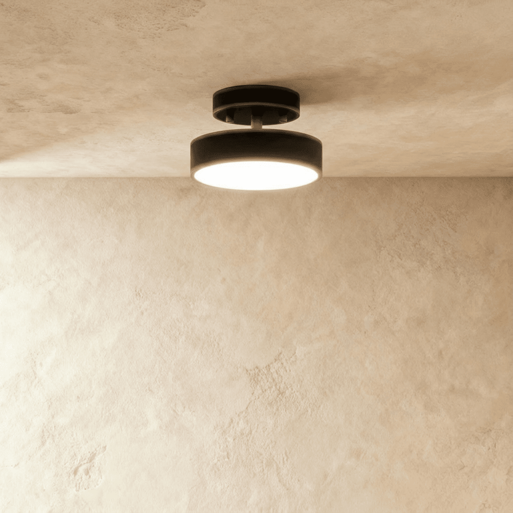Clérachic matte black flush-mount ceiling light with a warm frosted disc, shown centred on a plain plaster ceiling.
