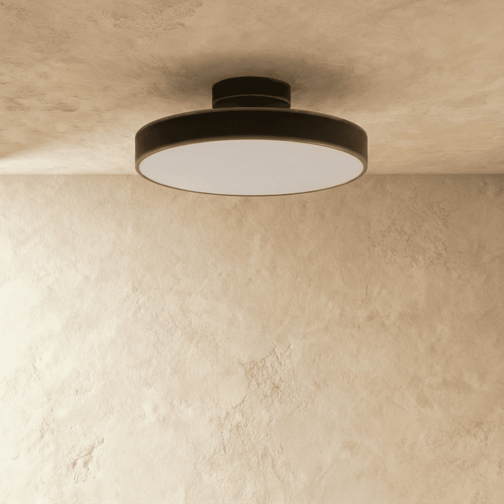 Clérachic black flush-mount ceiling light casting a soft warm glow from its round frosted lens in a plain room.