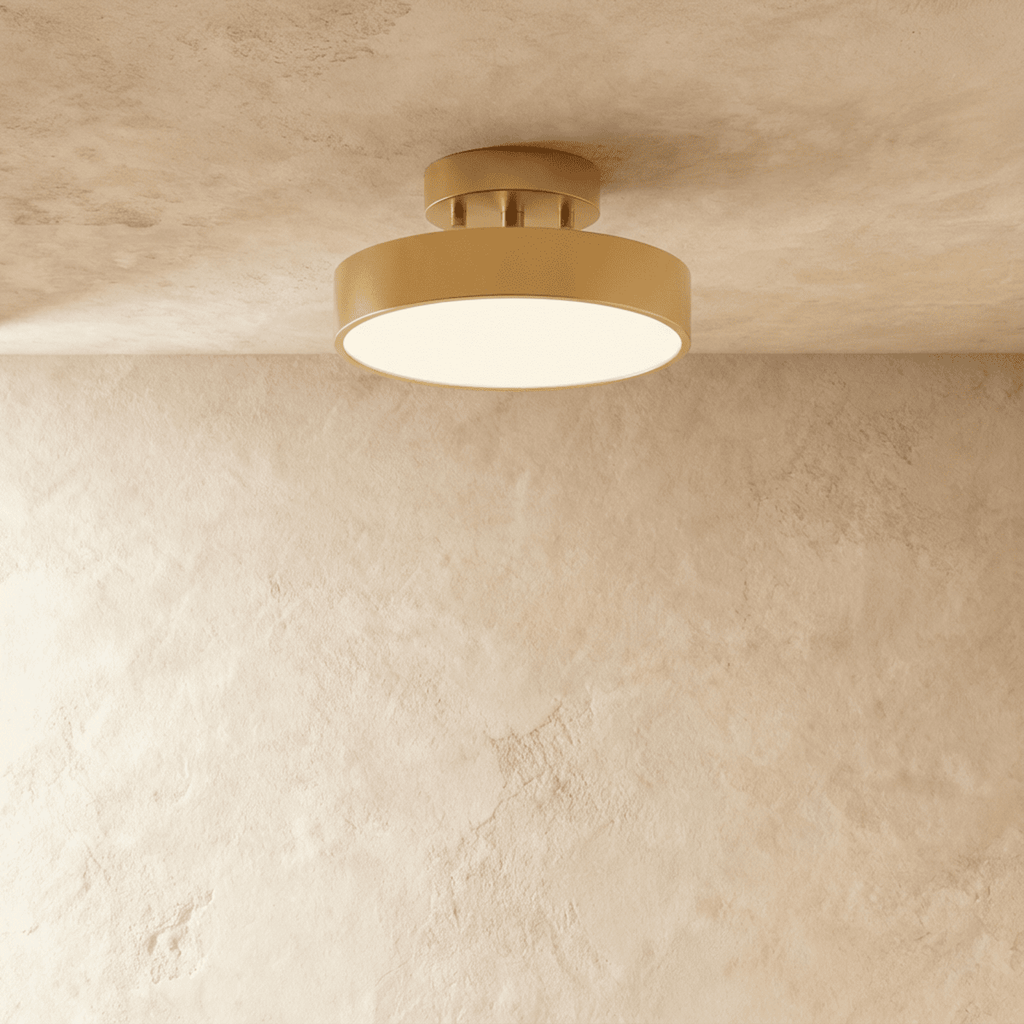 Clérachic copper flush-mount ceiling light glowing warmly, its brass drum shade set against a plain plaster wall.