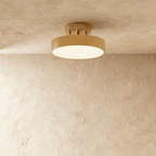 Clérachic copper flush-mount ceiling light glowing warmly, its brass drum shade set against a plain plaster wall.