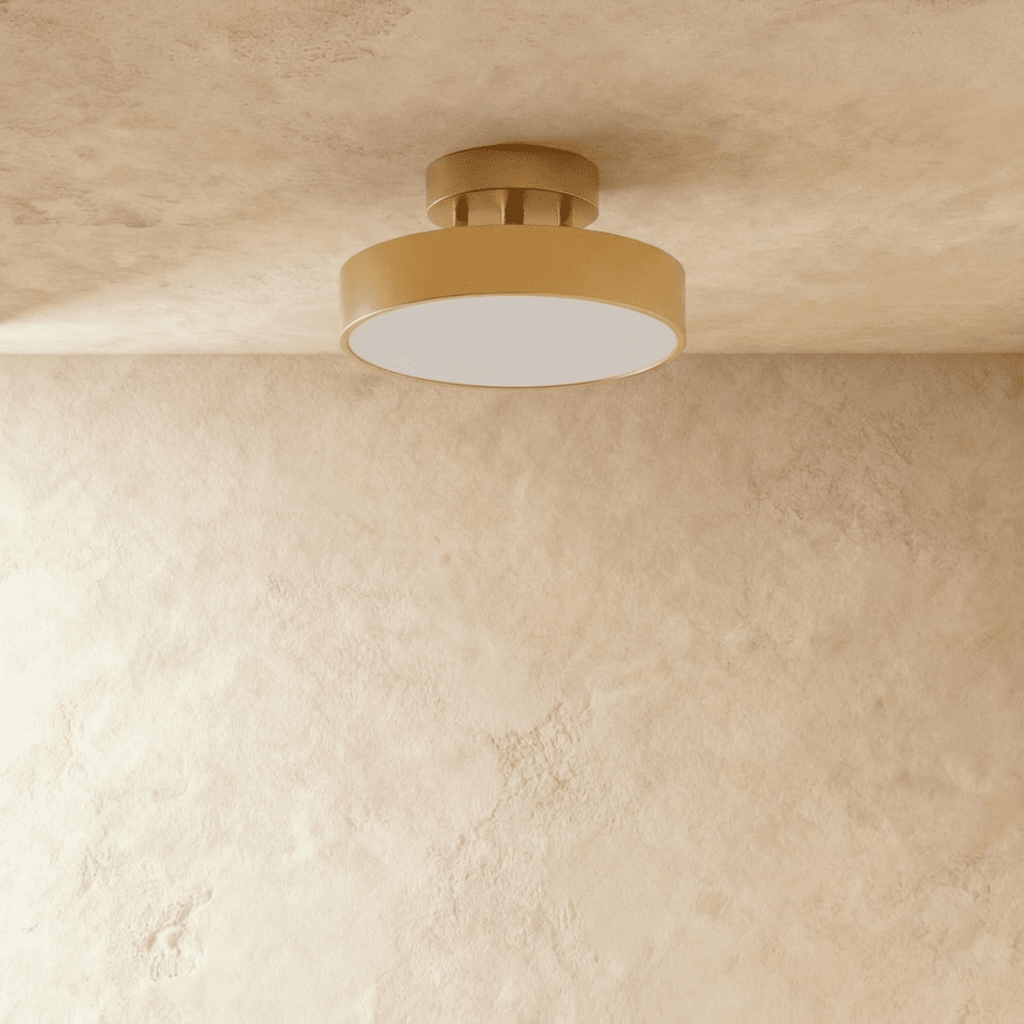 Clérachic copper flush ceiling light shown close, its brass drum and frosted disc glowing against a beige wall.