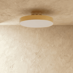 Clérachic copper ceiling light glowing warm, its brass drum shade mounted flush where wall meets plaster ceiling.