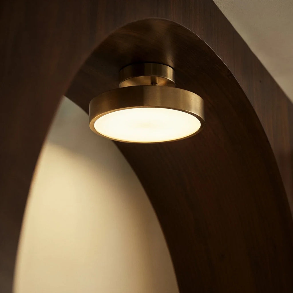 Clérachic copper flush-mount ceiling light shown close beneath a curved wood archway, its disc glowing warm white.