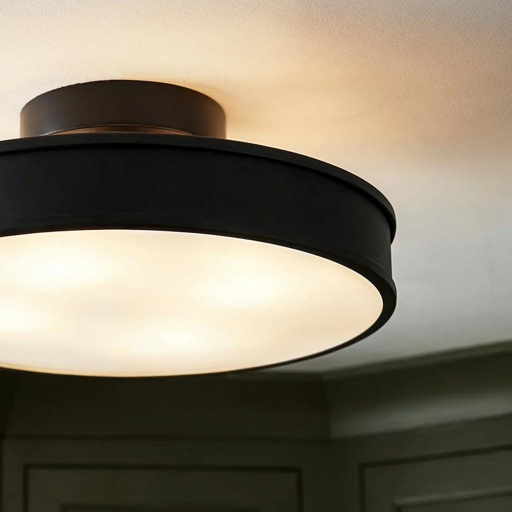 Clérachic black flush-mount light shown close up, its frosted disc glowing warm against a plain white ceiling.