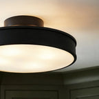 Clérachic black flush-mount light shown close up, its frosted disc glowing warm against a plain white ceiling.