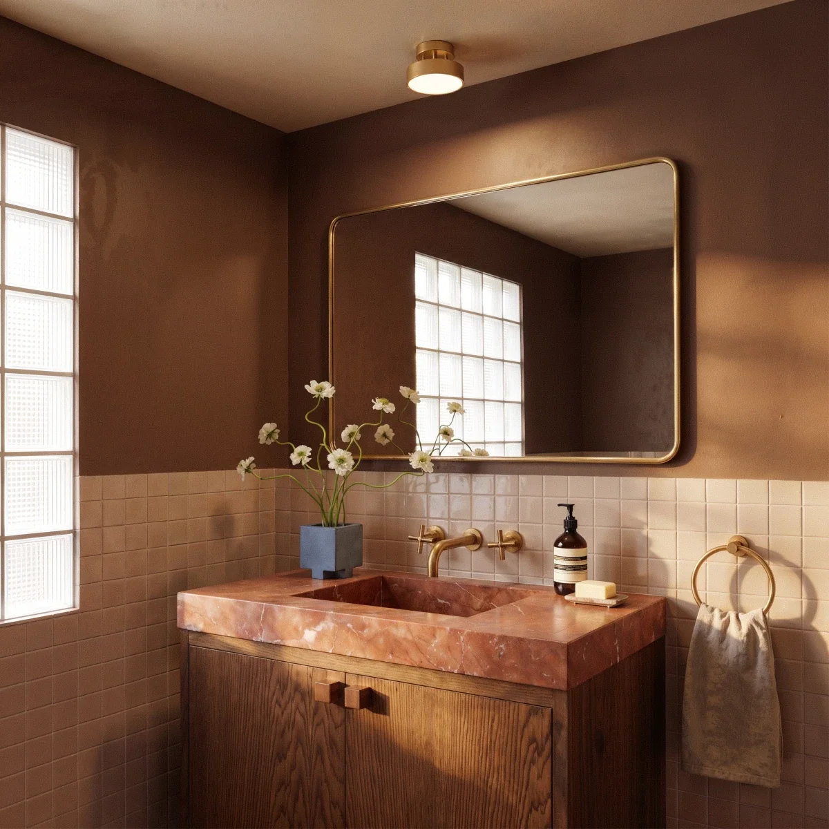 Clérachic copper flush-mount ceiling light glowing above a brass-framed mirror and marble vanity in a brown bathroom.