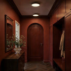 Clérachic black flush-mount ceiling lights glowing above a burgundy hallway with an arched door and herringbone floor.