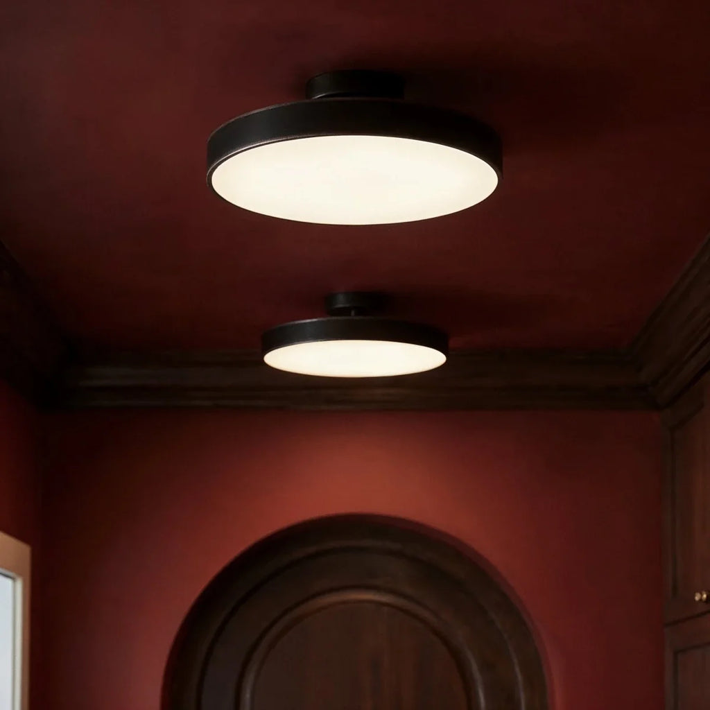 Clérachic black flush-mount ceiling lights shown close, their frosted discs glowing warm above a burgundy hallway.