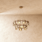 Clérachic chandelier in smoky bronze glass, its two tiers of cylinder shades lit against a plaster ceiling.