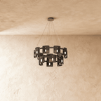 A larger two-tier Clérachic chandelier in dark smoky glass cylinders against a plaster wall.