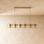 Clérachic linear chandelier with six amber glass cylinder shades along a slim bronze bar, each lit softly within.