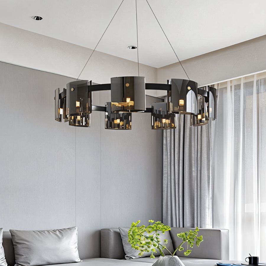 A Clérachic chandelier in dark smoky glass hangs low above a grey sectional sofa and sheer curtains.