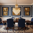 Clérachic crystal chandelier glowing over a mahogany dining table, with navy chairs and navy panelled walls hung with gilt-framed art.