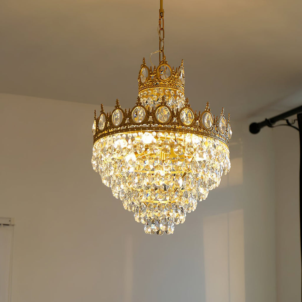 Lit Clérachic chandelier hung from a chain in a pale room, its crown-shaped copper-toned tiers full of clear crystal drops.