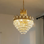 Lit Clérachic chandelier hung from a chain in a pale room, its crown-shaped copper-toned tiers full of clear crystal drops.
