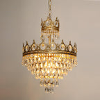 Clérachic crystal chandelier glowing against a soft grey wall, with a small crown tier above a larger one with teardrop crystals.