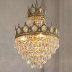 Close view of the crown-edged upper tier and layered crystal drops of this Clérachic chandelier, lit against a grey wall.