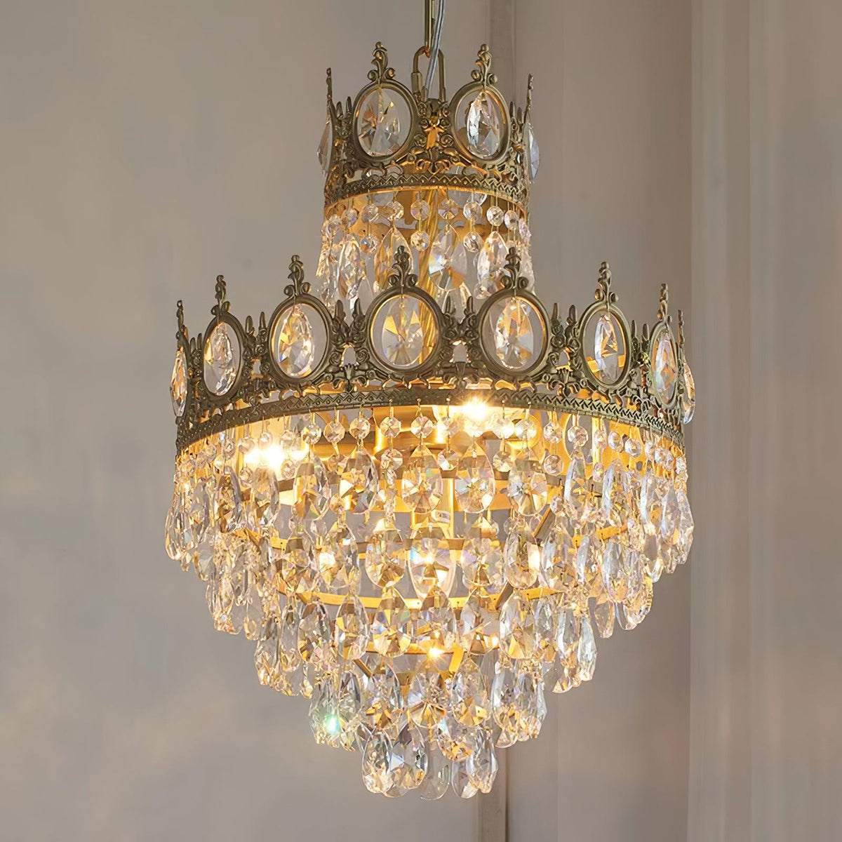 Close view of the crown-edged upper tier and layered crystal drops of this Clérachic chandelier, lit against a grey wall.